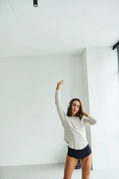 Attraktive brünette Frau in langen Ärmeln und Höschen tanzen, während sie Musik über Kopfhörer hört — Stockfoto