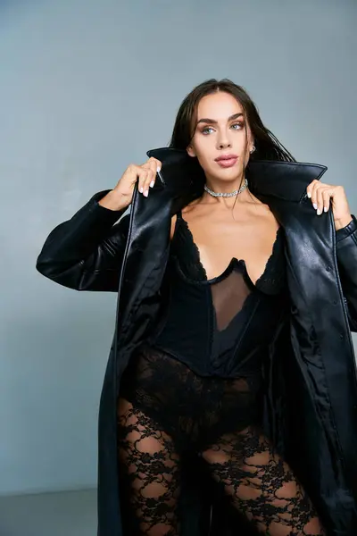 Mujer sexy con pelo mojado morena posando en abrigo de cuero negro y corsé mientras mira hacia otro lado - foto de stock