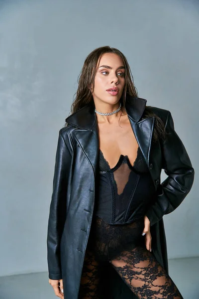 Mulher sexy com cabelo molhado morena posando em casaco de couro preto e roupa interior de renda, mão sobre quadril — Fotografia de Stock