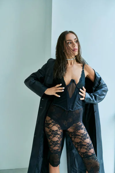 Femme passionnée avec des cheveux bruns posant en manteau de cuir et corset noir avec les mains sur les hanches — Photo de stock