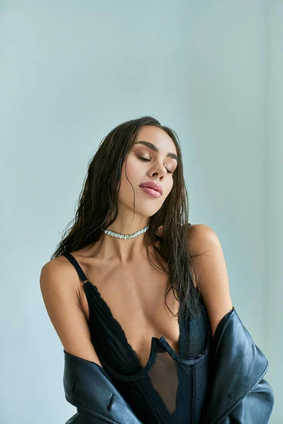 Sexy Frau mit nassen Haaren und geschlossenen Augen posiert in schwarzer Unterwäsche, Spitzenkorsett und Ledermantel — Stockfoto