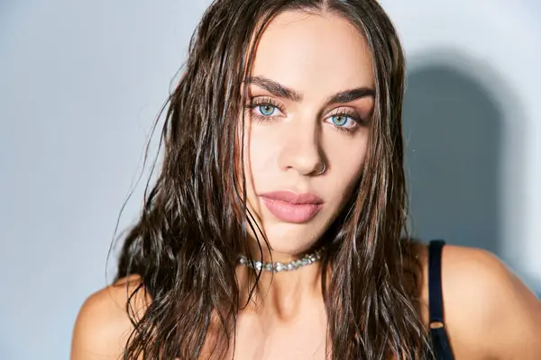 Porträt einer schönen Frau mit brünetten und nassen Haaren, die vor grauem Hintergrund in die Kamera blickt, blaue Augen — Stockfoto