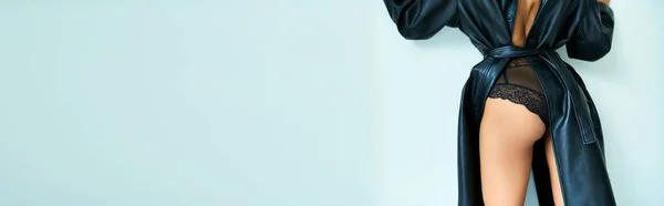 Mulher sexy cortada em casaco de couro com costas abertas e calcinhas de renda de pé perto da parede cinza, banner — Fotografia de Stock