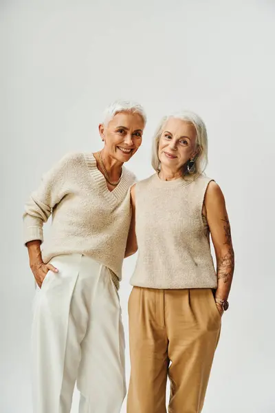 Reife Damen in stylischer Pastellkleidung posieren mit Händen in Taschen auf grau, Eitelkeit fair Stil — Stockfoto