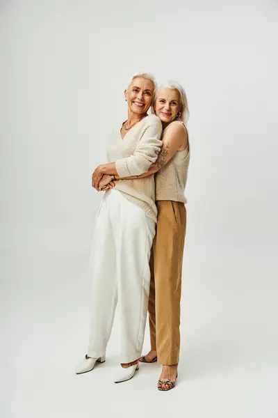Glücklich tätowierte Frau umarmt stilvolle Freundin auf grau, anmutige Alterung der älteren Modelle — Stockfoto