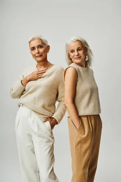 Ältere Damen in trendiger Freizeitkleidung, die Hände in Taschen auf grauer, lebenslanger Freundschaft stehend — Stockfoto