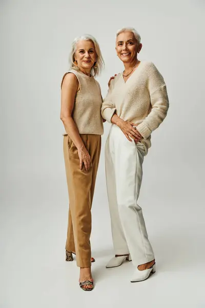 Full length of cheerful mature women in elegant casual clothes smiling at camera on grey backdrop — Stock Photo