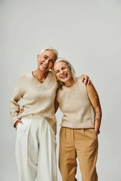 Cheerful mature ladies in trendy pastel embracing and looking at camera on grey, lifelong friends — Stock Photo