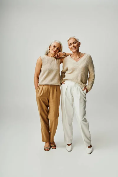 Volle Länge der Smiley-Senior-Models in pastellfarbener Freizeitkleidung stehend mit Händen in Taschen auf grau — Stockfoto