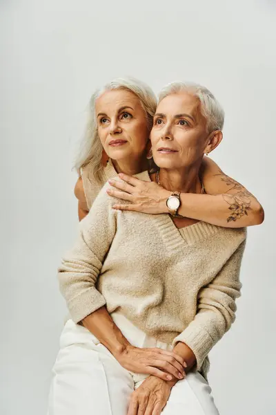 Senior tattooed woman embracing dreamy female friend looking away on grey, elegant lifestyle — Stock Photo