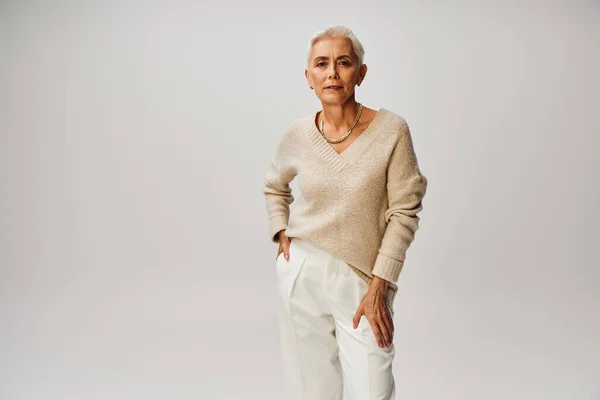 Confident senior fashionista with silver hair posing with hand in pocket of white pants on grey — Stock Photo