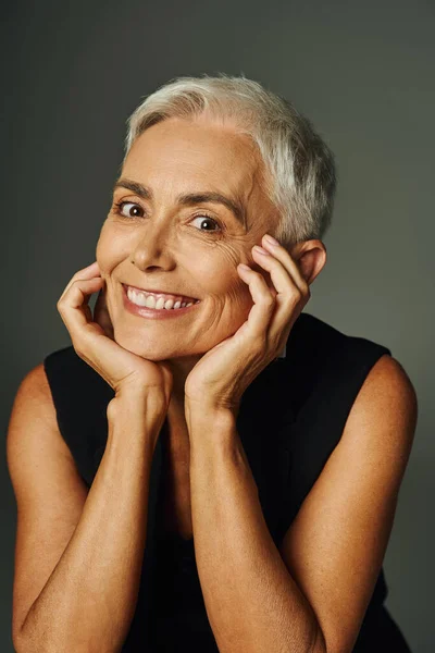 Portrait of joyful senior lady with short silver hair looking at camera on grey, elegance and charm — Stock Photo