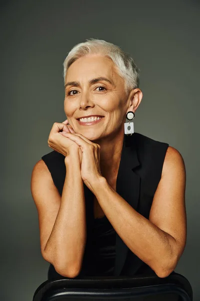 Porträt einer trendigen Seniorin, die mit den Händen vor dem Gesicht posiert und vor grauem Hintergrund in die Kamera lächelt — Stockfoto