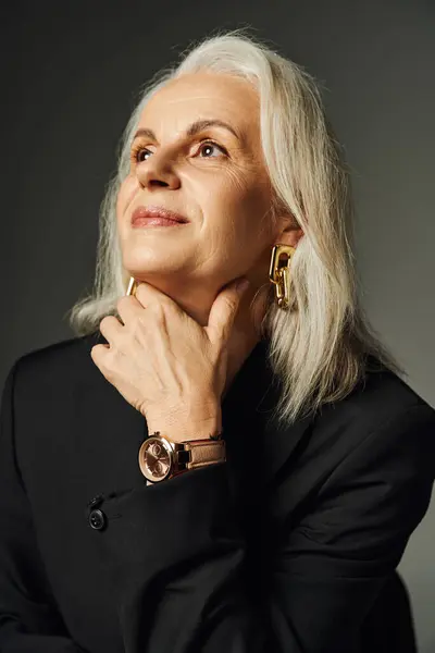 Portrait de dame âgée rêveuse et élégante en montre-bracelet et accessoires dorés regardant loin sur gris — Photo de stock
