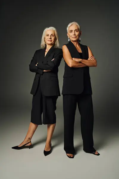 Senior fashion photography, elegant ladies in black clothes posing with folded arms on grey backdrop — Stock Photo