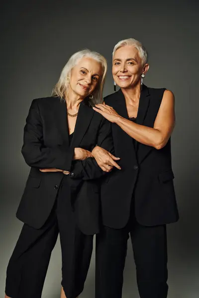 Happy and fashionable senior female friends in black clothes looking at camera on grey, age positive — Stock Photo