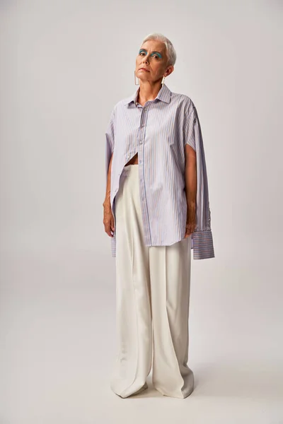 Longitud completa de la señora madura de moda en pantalones cortos y blancos de rayas azules sobre fondo gris - foto de stock