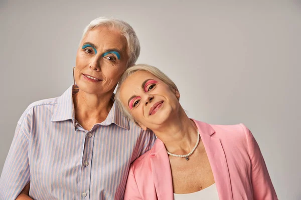 Joyful senior female friends in trendy blue and pink attire looking at camera on grey, happiness — Stock Photo