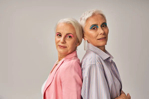 Гламурні старші жінки в стильному синьо-рожевому одязі, що стоїть назад на сірому тлі — стокове фото