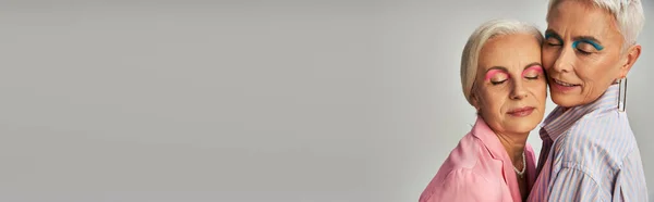 Senior lifelong female friends with silver hair and makeup standing with closed eyes on grey, banner — Stock Photo