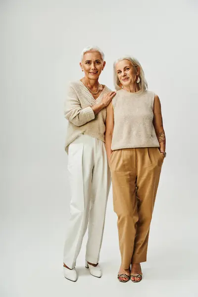 Piena lunghezza di felici amiche anziane in abiti alla moda pastello in piedi su sfondo grigio — Foto stock