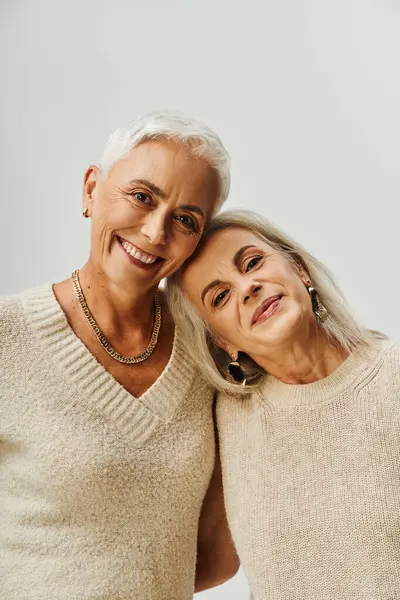 Портрет усміхнених старших жінок у макіяжі та золотих аксесуарах, які дивляться на камеру на сірому фоні — стокове фото