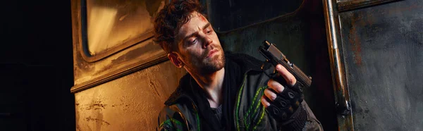 Mann mit verletztem Gesicht blickt auf Waffe in verlassener U-Bahn, postapokalyptischer Überlebender, Transparent — Stockfoto