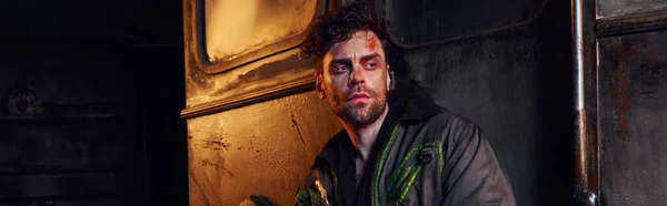 Uomo disperato in giacca indossata guardando lontano nel buio della metropolitana devastata post-apocalittica, striscione — Foto stock