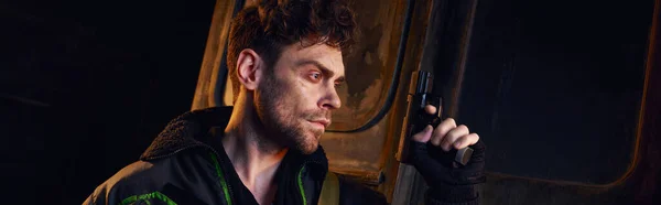 Unrasierter Mann in verschlissener Jacke mit Waffe im dunklen Untergrund, postapokalyptisches Konzept, Banner — Stockfoto