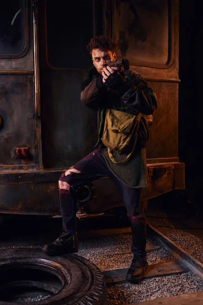 Игровой персонаж в изношенном наряде, нацеленный с оружием в заброшенном метро, постапокалиптическое выживание — стоковое фото