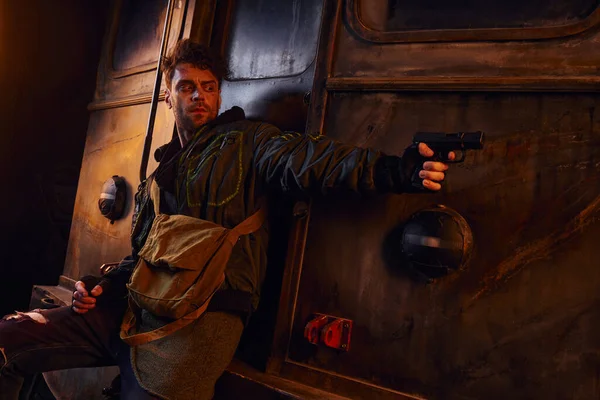 Небезпечний чоловік ховається за вагоном і прицілюється з пістолетом у покинутому метро, після катастрофи виживання — стокове фото