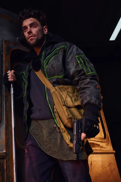 Небезпечний чоловік з подряпаним обличчям, що стоїть з мішком для полотна та пістолетом у небезпечному після катастрофи метро — стокове фото