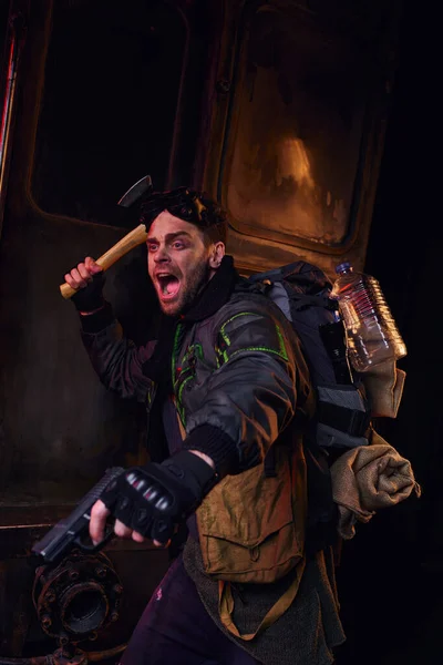 Hombre gritando armado con hacha y arma defendiendo en metro abandonado, supervivencia post-apocalíptica - foto de stock