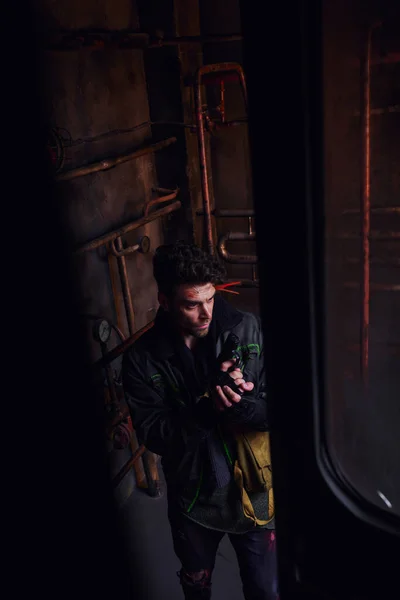 Vista de alto ángulo del hombre en ropa gastada de pie con pistola en el túnel subterráneo post-apocalíptico - foto de stock