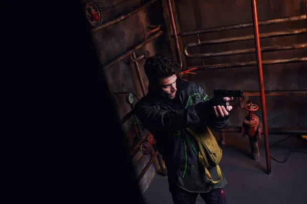 Uomo concentrato puntando con la pistola in metropolitana abbandonata vicino condutture arrugginite, personaggio del gioco — Foto stock