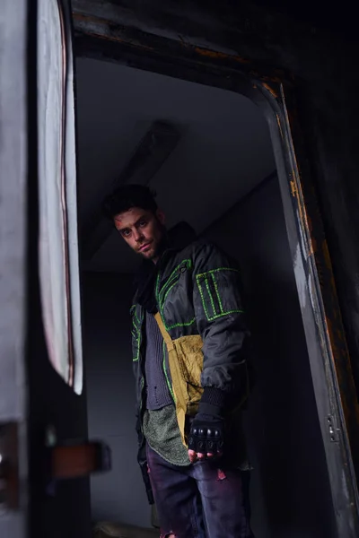 Düsterer Mann in schwarzer Jacke, der in verlassenen U-Bahn-Waggons in die Kamera blickt, postapokalyptisches Konzept — Stockfoto