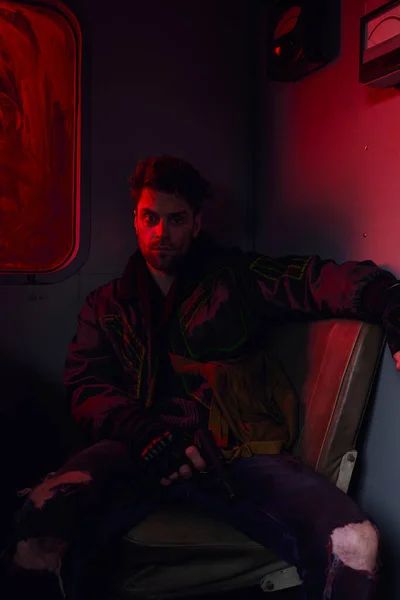 Hombre deprimido con el arma sentado en el vagón abandonado del metro en la luz roja, concepto post-apocalíptico - foto de stock