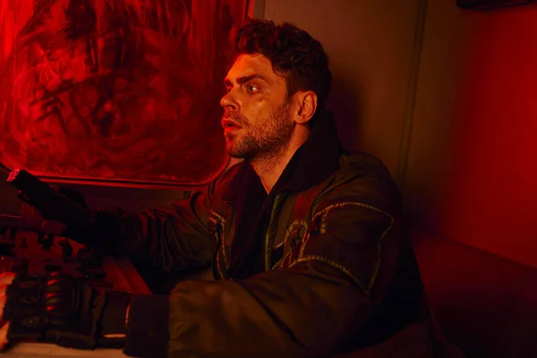 Angespannter Mann mit Waffe sitzt in schmutzigem Wagen in verlassener U-Bahn im Rotlicht, Leben nach der Apokalypse — Stockfoto