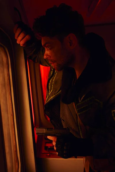 Uomo armato che guarda attraverso sporchi finestrini della metropolitana abbandonata, sopravvivenza post-apocalittica — Foto stock