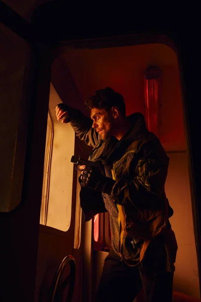 Man with gun standing near window of abandoned carriage in post-apocalyptic subway with red light — Stock Photo