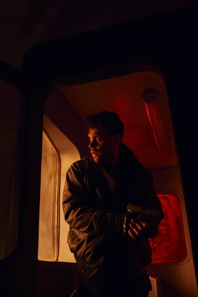 Концентрированный человек с пистолетом, смотрящий на камеру в вагоне метро после катастрофы в красном свете — стоковое фото