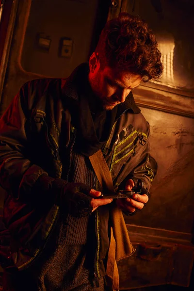 Homme en tenue usée regardant manomètre dans un wagon de métro avec lumière rouge, post-apocalypse — Photo de stock