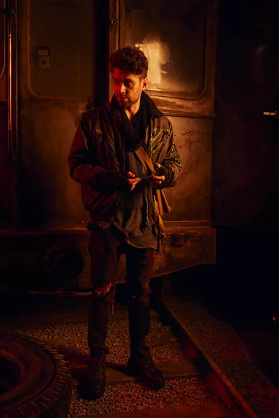 Uomo in abiti sporchi con pezzo di ricambio di carrozza arrugginita in metropolitana post-disastro con luce rossa — Foto stock