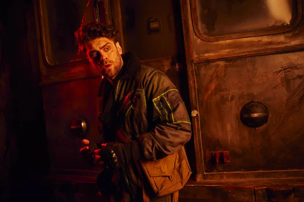 Испуганный человек смотрит в сторону заброшенного вагона метро в красном свете, концепция постапокалипсиса — стоковое фото