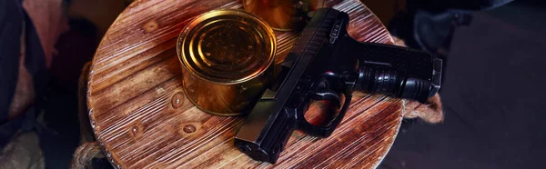 Top view of gun and canned food in tin on barrel in underground, post-apocalyptic resources, banner — Stock Photo