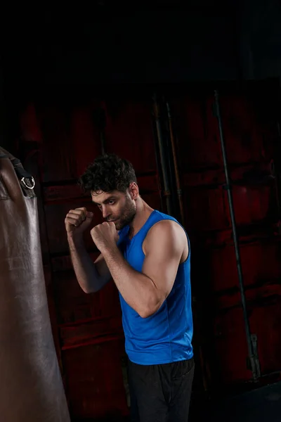 Unshaven man in sportswear training with punching bag in city at night — Stock Photo