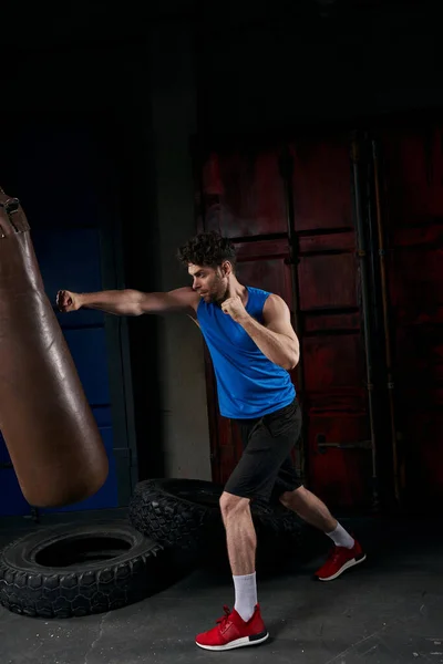 Full length of confident athletic man in sportswear training with punching bag on street at night — Stock Photo