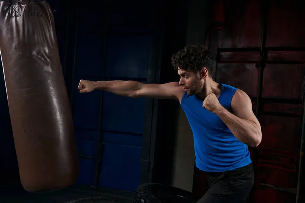 Unshaven sportive man boxing punching bag in darkness on urban street, outdoor workout — Stock Photo