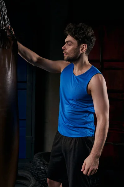 Sportlicher Mann in blauem Tanktop steht nachts neben Boxsack auf der Stadtstraße — Stockfoto