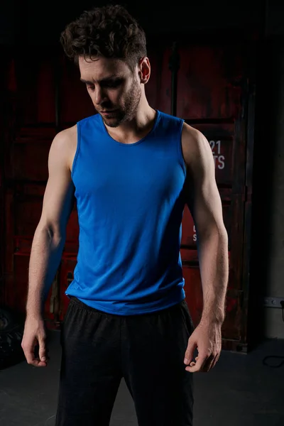 Unshaven athletic man in blue tank top standing in darkness on city street at night — Stock Photo